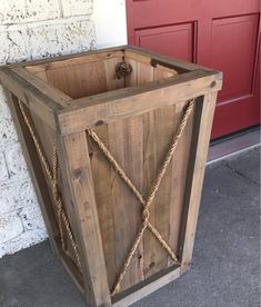 a wooden box sitting on the ground next to a red door with rope wrapped around it