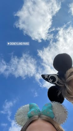 a woman is wearing mickey ears and looking up at the sky with clouds in the background