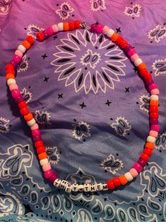 a pink and orange beaded necklace sitting on top of a purple cloth covered bed