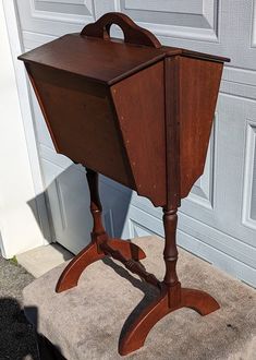 an old fashioned wooden stand with a magazine holder on it's legs, sitting in front of a garage door