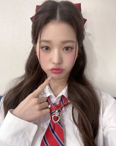 a girl in a white shirt and red tie is posing for the camera with her finger on her lips