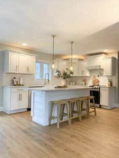 a large kitchen with white cabinets and wood flooring is pictured in this image, there are two stools on the island