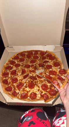 a pepperoni pizza sitting in a box on the floor with someone cutting into it