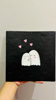 a person holding up a black and white painting with hearts on it's face