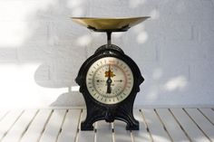 an old fashioned clock sitting on top of a wooden table next to a white brick wall