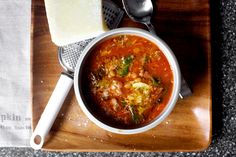 a bowl of soup on a wooden tray with two spoons next to it and cheese