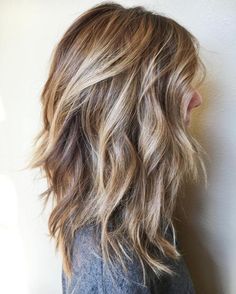 the back of a woman's head with long, wavy hair and brown to blonde highlights