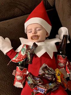 a baby dressed as santa claus is sleeping with candy and beer in his mouth while wearing an elf costume