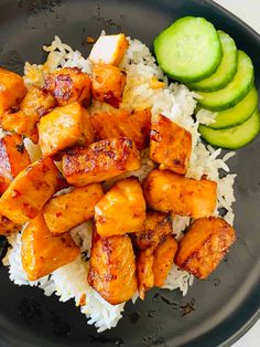 chicken and rice with cucumber on the side in a black plate, ready to be eaten