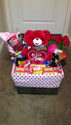 a red teddy bear sitting on top of a box filled with candy