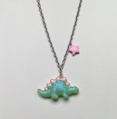 Pastel green stegosaurus necklace with glitter and pink accents on a silver chain with a pink star charm. Playful Adjustable Silver Charm Necklace, Playful Adjustable Silver Necklace, Green Sterling Silver Charm Necklace With Lobster Clasp, Pink Star-shaped Sterling Silver Jewelry, Cute Silver Jewelry With Star Charm, Cute Silver Star Jewelry, Pink Star Charm Pendant Jewelry, Green Nickel-free Pendant Charm Necklace, Adjustable Green Sterling Silver Charm Necklace