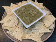 some tortilla chips are on a plate with a small bowl of green salsa