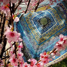 a blue and yellow blanket sitting on top of a green field next to pink flowers