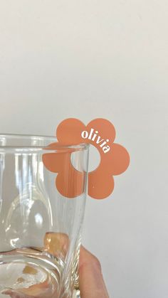 a person holding up a glass with a flower on the top and an orange sticker