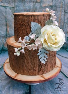 a three tiered chocolate cake with white flowers and leaves on the top is sitting on a wooden stand