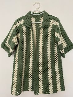 a green and white crocheted sweater hanging on a hanger, with an open collar