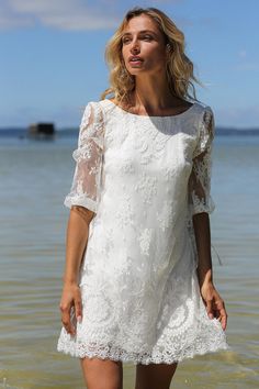 a woman is standing in the water wearing a white dress with sheer sleeves and an open back