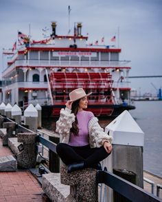 a woman is sitting on the edge of a pier with a boat in the background