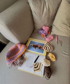 there are many crocheted items on the couch next to an open book and hat