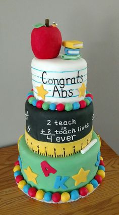 a three tiered cake has an apple on top and school supplies on the bottom