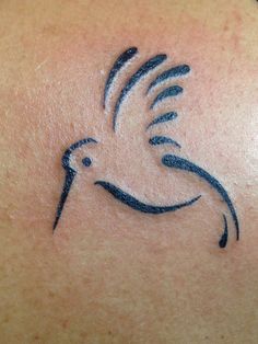 a small tattoo on the back of a woman's shoulder, with a bird in flight