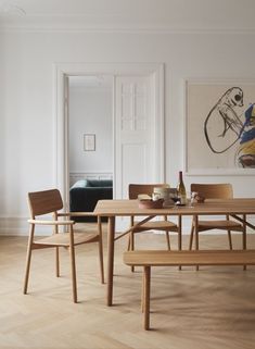 a wooden table with two chairs and a bench in front of it, next to a painting on the wall