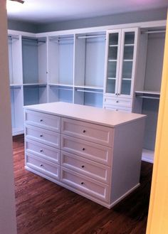 an empty room with white cabinets and drawers in the center, on hard wood flooring