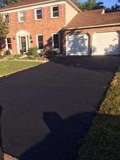 a driveway with a black tarmac in front of a brick house on a sunny day