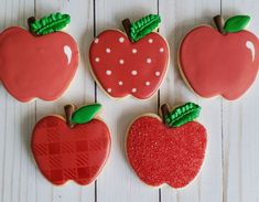 four decorated apple cookies sitting on top of a white wooden table next to each other