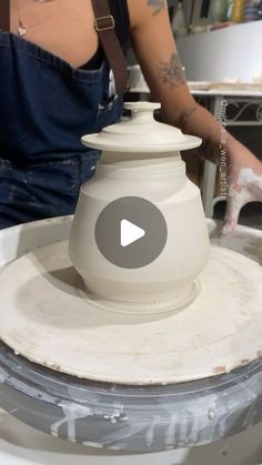 a woman is making a vase out of clay and white paint on top of a table