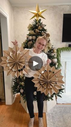 a woman standing in front of a christmas tree holding two paper stars and pointing at the camera