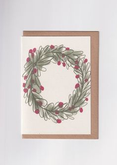 a card with a wreath on it and red berries hanging from the front, sitting on top of a white surface