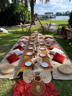 a long table set up with plates and place settings for dinner on the grass near water