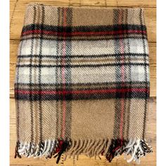 a plaid blanket is laying on top of a wooden floor and it has tassels around the edges