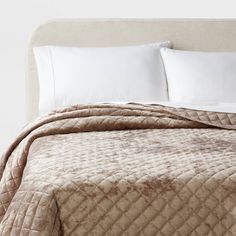 an unmade bed with white pillows and brown quilted bedspread on it