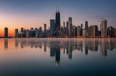 the city skyline is reflected in the water at sunset or dawn, as seen from across the bay