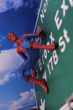 a close up of a toy spider man on a street sign with clouds in the background