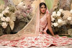 a woman sitting on the ground in a bridal gown with flowers around her neck