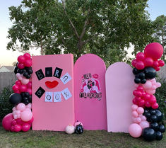 a pink and black birthday decoration with balloons on the top, in front of a tree