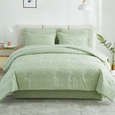 a bed with green comforter and pillows in a room next to a plant on the floor