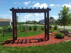 a wooden swing set sitting in the middle of a lush green field