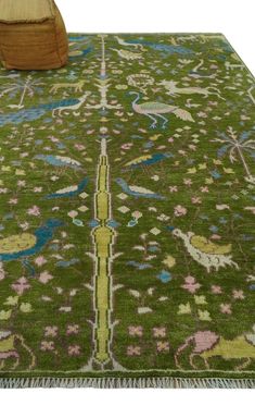 a green rug with blue, pink and yellow designs on the ground next to a wooden chair