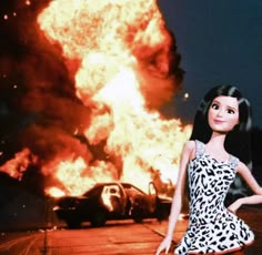 a barbie doll standing in front of a burning car