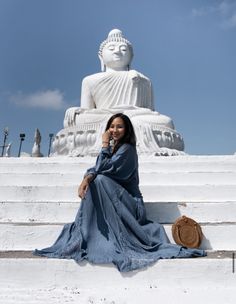 a woman is sitting on the steps in front of a large buddha statue and talking on her cell phone