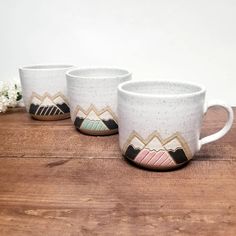 three coffee mugs sitting on top of a wooden table