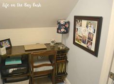 a desk with pictures hanging on the wall and a lamp next to it in a room