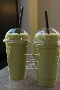 two green smoothies in plastic cups with straws on top, sitting next to each other