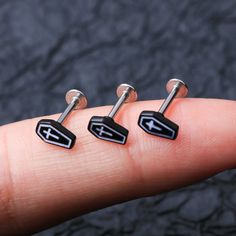 three pairs of black and silver ear studs with arrows on each end, in front of a dark background