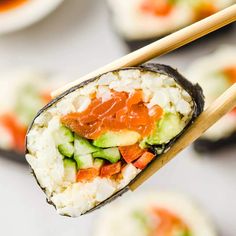 chopsticks holding sushi with cucumber and tomato on them, ready to eat