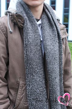 a young man wearing a gray scarf and brown jacket standing in front of a building